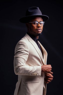 Beyaz ceketli, gözlüklü, stüdyodaki siyah arka planlı yakışıklı Afro-Amerikan melankolik çocuk. Gizem ve keder.