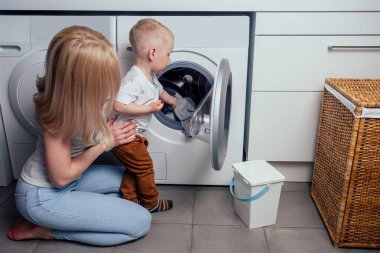 Mutlu aile evi hafta sonu sabah banyo yıkama makinesi. Anne ve küçük oğlu çamaşır odasında çamaşır yıkıyor.