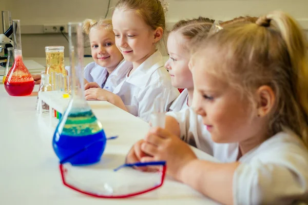 Grupo de niños de la escuela con el profesor en el laboratorio de la escuela haciendo experimento observando la reacción química con el tinte con vinagre y el volcán de soda con vestido blanco de vidrio uniforme — Foto de Stock