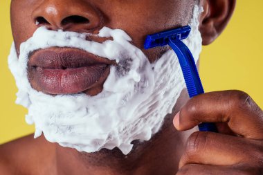 Yüzünde tıraş köpüğü ve jileti olan Afro-Amerikalı bir adam.