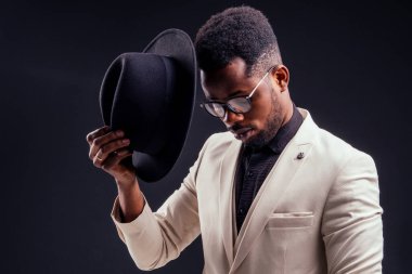 Beyaz ceketli, gözlüklü, stüdyodaki siyah arka planlı yakışıklı Afro-Amerikan melankolik çocuk. Gizem ve keder.