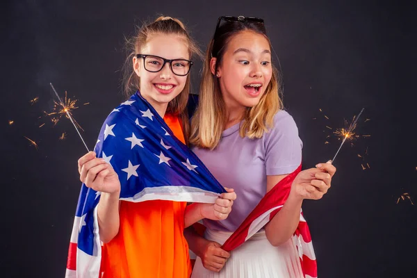group of Asian and European friends laughing girls wrapped in american flag spring party summer style black background studio, visa and independence day usa