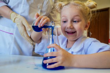 Gözlüklü ve beyaz tıp önlüklü zeki sarışın kimyager bilim deneyleri kimyası yapıyor, laboratuvar sınıfında farklı kimyasal çözümleri karıştırıyor.