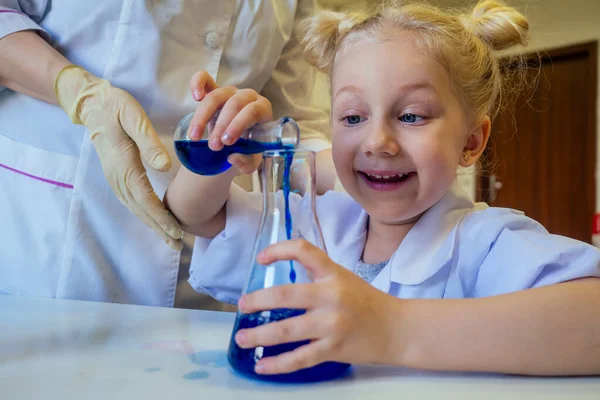 surprised and amazed clever blonde school girl chemist in eyeglasses and white medical gown making science experiments chemistry ,mixing different chemical solutions in laboratory classroom