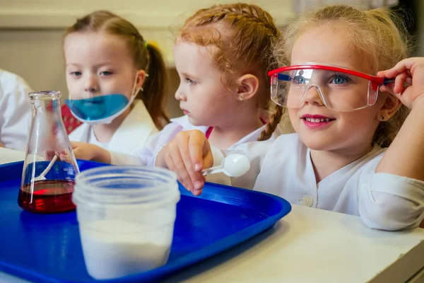 Группа школьниц с учителем в школьной лаборатории проводят эксперимент, наблюдая химическую реакцию с красителем с уксусом и содовым вулканом в белом халате — стоковое фото