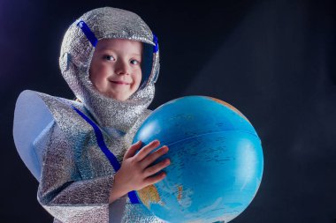 Mutlu kostümlü astronot kız stüdyoda siyah bir arka planda dünyayı tutuyor.