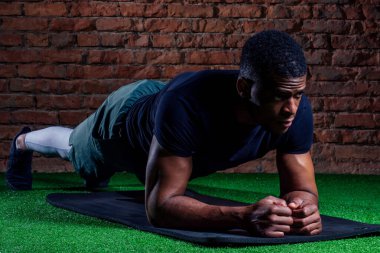 Genç kaslı Afrikalı Amerikalı adam şınav çekiyor ve başka tarafa bakıyor.