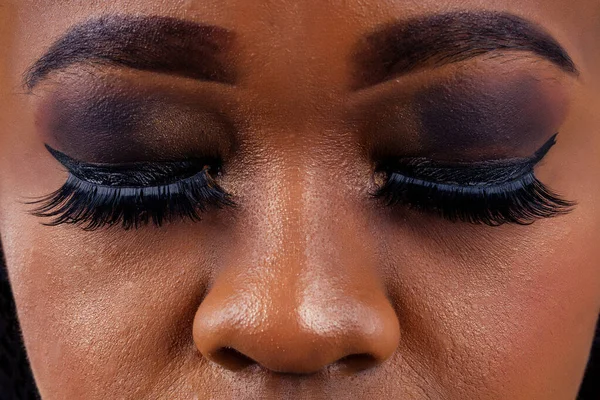 Αφρικανή γυναίκα με επαγγελματική απαρτίζουν Smokey μάτια κλειστά μακριά βλεφαρίδες ψευδείς, σκούρες σκιές στα βλέφαρα και τα φρύδια κοσμετολόγος — Φωτογραφία Αρχείου