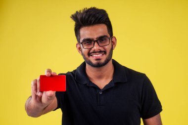 Stüdyoda sarı arka planda plastik kart tutan bir öğrenci.