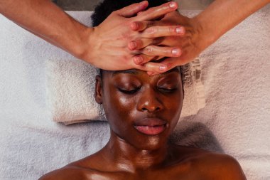 Güzel afro-amerikan kadın Ayurveda yüz masajı yaptırıyor spa salonundaki beyaz tenli adam tarafından..