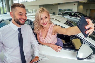 Mutlu çift, yeni arabasının önünde dikiliyorlar. Karısının gözleri ile showroom 'daki akıllı telefon kamerasında selfie çekiyorlar. Sürpriz araba hediyesi.