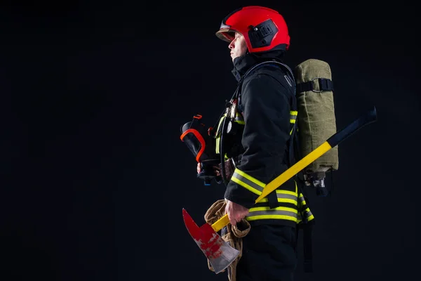 Портрет сильного пожежного у вогнетривкій формі, що тримає сокиру в руках чорна фонова студія — стокове фото