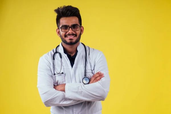 Indický lékař nosí brýle a bílý plášť ve žlutém pozadí studia — Stock fotografie