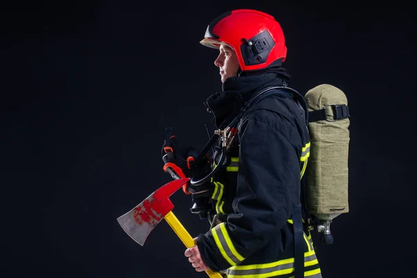 Retrato forte bombeiro em uniforme à prova de fogo segurando um machado em suas mãos preto fundo estúdio — Fotografia de Stock