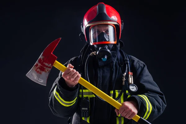 Retrato forte bombeiro em uniforme à prova de fogo segurando um machado em suas mãos preto fundo estúdio — Fotografia de Stock