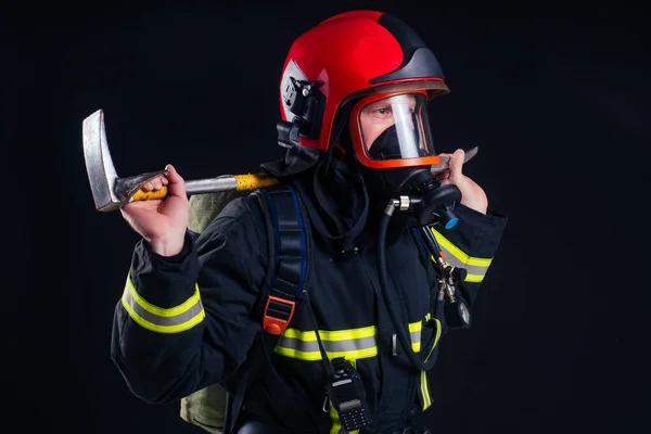 Retrato forte bombeiro em uniforme à prova de fogo segurando um machado em suas mãos preto fundo estúdio — Fotografia de Stock