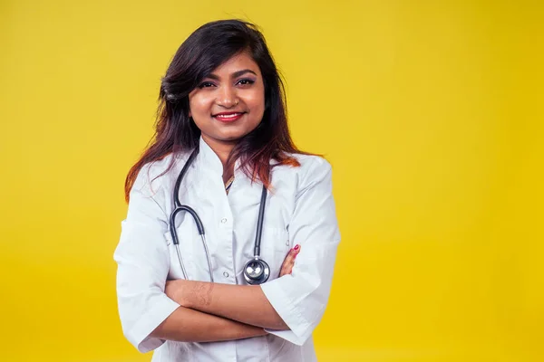 Mulher indiana jovem e bonita mulher loira ginecologista médico usando estetoscópio em um casaco médico branco em um fundo amarelo no estúdio — Fotografia de Stock