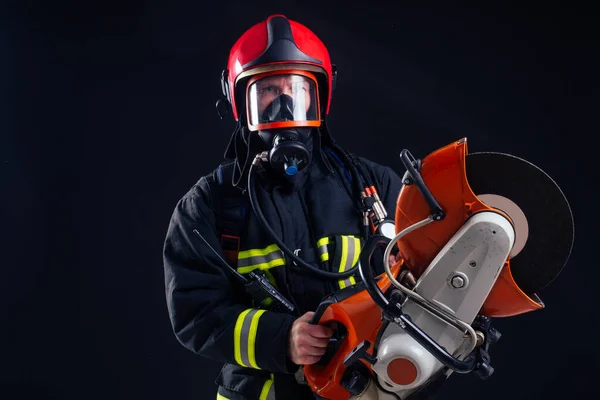 Portrait strong fireman in fireproof uniform holding an ax chainsaw in his hands black background studio — Stock Photo, Image