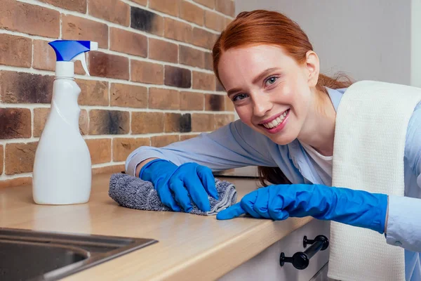 Caucasico sorridente donna dai capelli rossi che lavora in cucina in abiti casual e guanti di gomma — Foto Stock