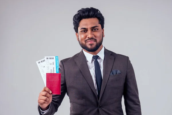 happy indian student male bearded wearing stylish classic suit holding passport airline ticket white studio background . lifestyle summer trip concept