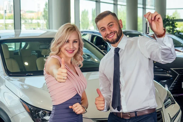 Feliz pareja de pie en frente de coche nuevo, hombre cubierto de ojos de esposa en showroom.surprised regalo automóvil — Foto de Stock