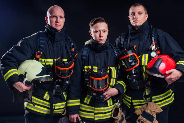 Retrato forte bombeiro em uniforme à prova de fogo segurando um machado motosserra em suas mãos preto fundo studio.team trabalho conceito — Fotografia de Stock