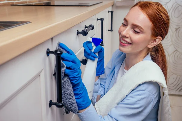 Caucasico bella donna con la testa rossa in abiti casual indossando guanto di gomma e tenendo spray chemica in cucina — Foto Stock