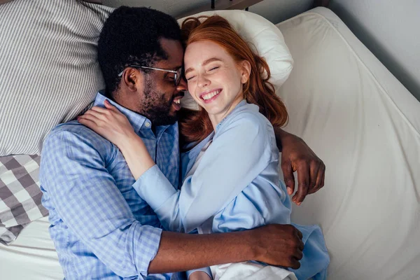 ginger hair european female and handsome afro african male together hugging lying in bedroom at home cozy apartment