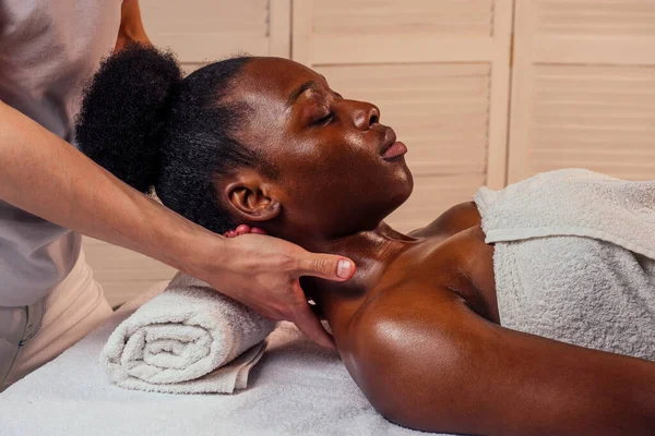 Vacker afrikansk amerikansk kvinna får Ayurveda ansiktsmassage av vithyade händer man i spa salong. — Stockfoto