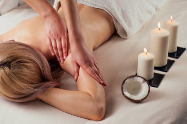 Ayurvedic rahatlatıcı. Sağlık güzeli mutlu sarışın kadın masaj yaptırıyor. Güzel kız spa merkezinin keyfini çıkarıyor, mum ateşinin yanındaki masa tedavisi prosedürünün üzerine uzanıyor.
