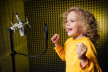 girl blonde curly hair style star singer artist in a yellow blouse with headphone recording new song with microphone. clipart