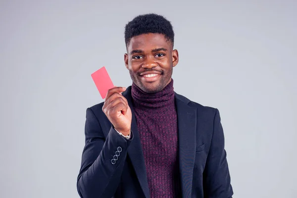 Elegante afroamericano en traje pantalones negros y chaqueta con un cuello de camisa grande sosteniendo tarjeta de plástico de crédito rojo en el estudio sobre fondo blanco, insignia mi nombre es —  Fotos de Stock