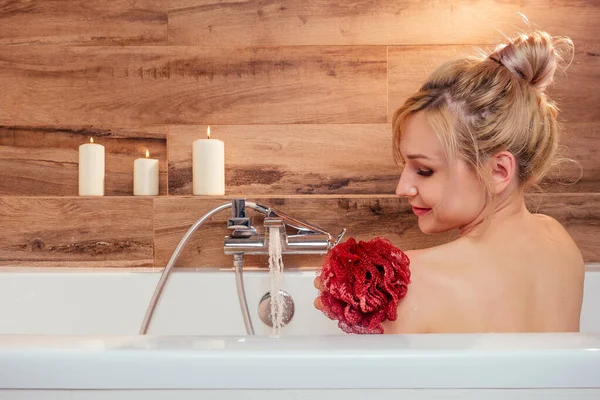 Preciosa joven sosteniendo una esponja roja relajándose en el baño — Foto de Stock