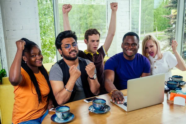 Multinationell grupp glada vänner njuta och dricka te café tittar på bärbara bildskärmen och jublar . — Stockfoto