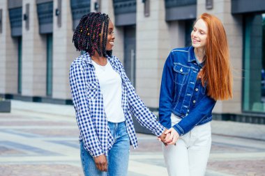 Neşeli afro ve Avrupalı lezbiyen kadınlar yazın şehir merkezinde gülüyor ve kameraya bakıyor.