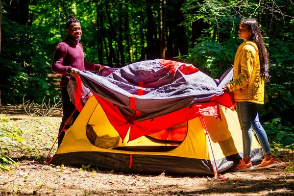 Afro americano misto casal estabelecendo instalação de uma barraca e tendo um tempo de descanso ao ar livre — Fotografia de Stock