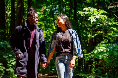 Afrika kökenli Amerikalı erkek ve melez Asyalı kadın parkta yürüyorlar.