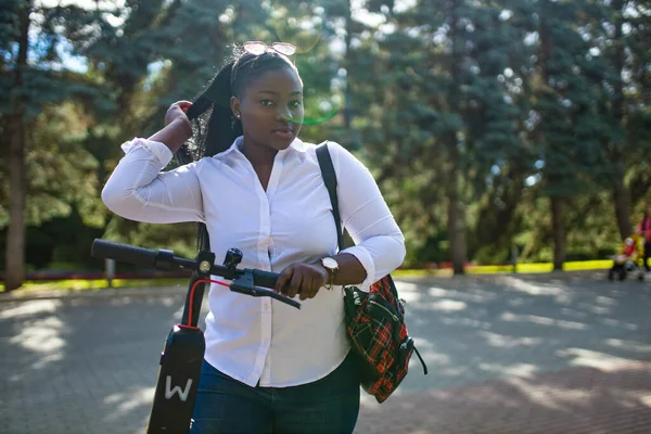 Mulher de raça mista montando uma scooter elétrica no verão na rua — Fotografia de Stock