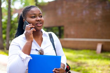 Güzel gülümseyen Afrikalı bir kadın beyaz tişört giyiyor ve elinde bir defter tutuyor.