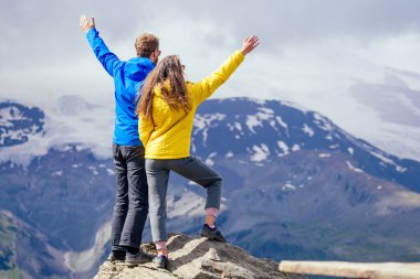Sarı ve mavi yağmurluklu iki genç yürüyüşçü Elbrus 'taki dağlarda dikiliyorlar.