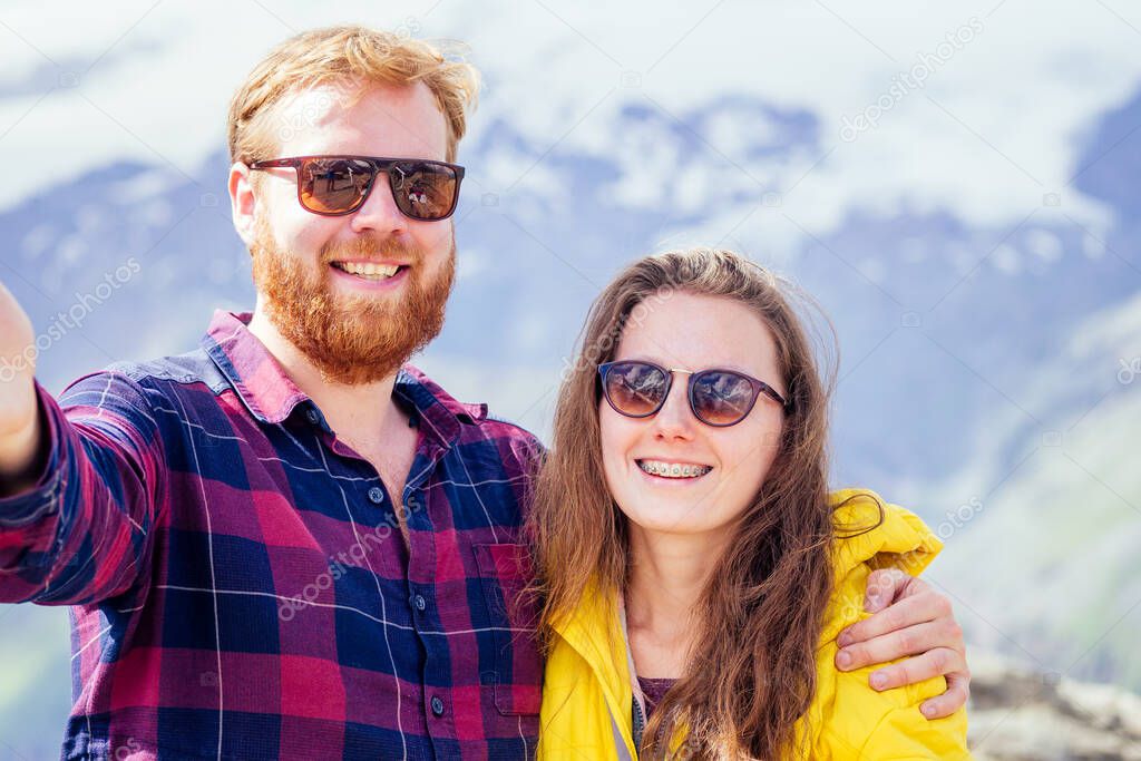 Couple of young hikers in yellow and blue raincoats standing on mountains in Elbrus