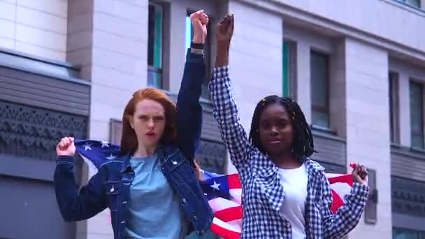 Червоноволоса імбирна жінка і африканська жінка, що тримає прапор США в центрі міста. — стокове відео