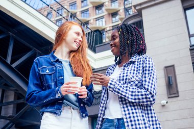 Kızıl saçlı kızıl kadın ve Brezilyalı kız arkadaşı yaz parkında sokakta kakao içiyorlar.