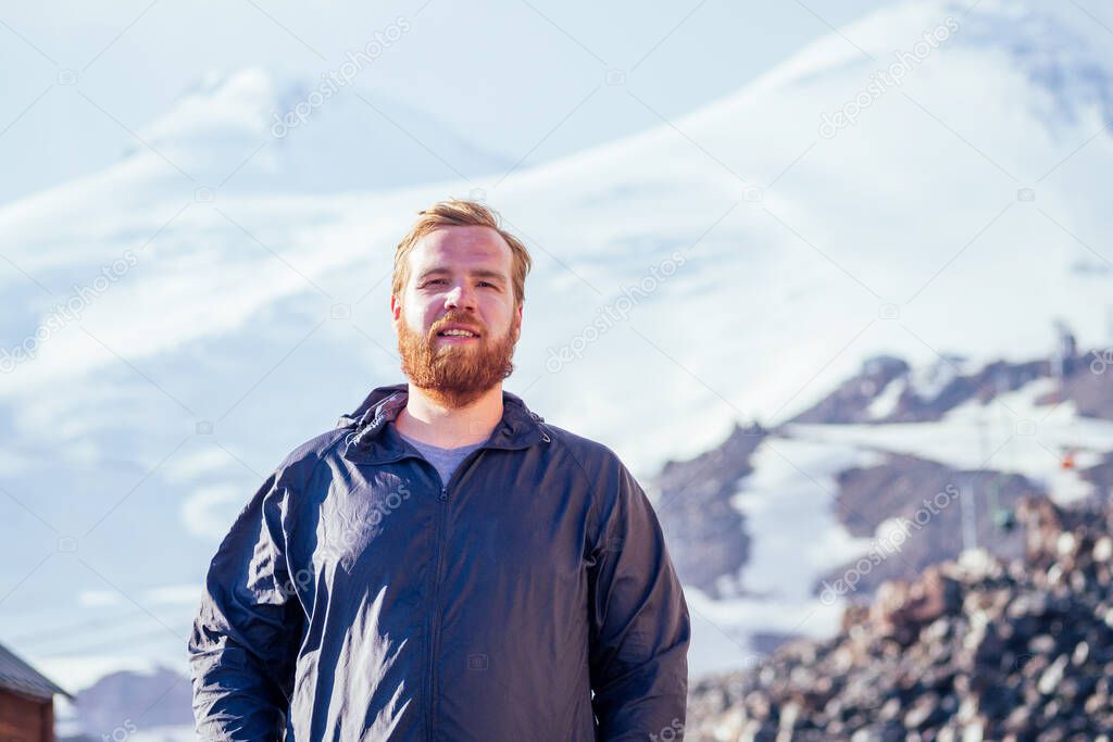 portrait of a young man with a beard on the background of mountains