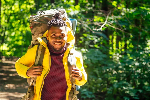 Homem americano africano em casaco amarelo com saco de licitação em sholders de volta na floresta — Fotografia de Stock