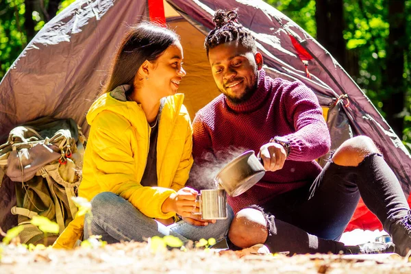 Hombre afroamericano y mujer hispana bebiendo té, cocinando comida en un quemador de gas — Foto de Stock