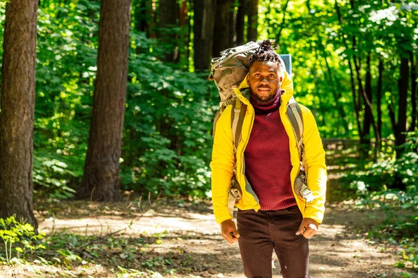 African american man in yellow jacket with bid bag in sholders back in the forest — Stock Photo, Image