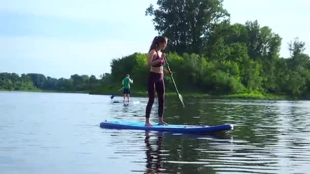 Жінка штовхає і тягне весло крізь сяючу поверхню води і провідну дошку в сонячний ранок — стокове відео