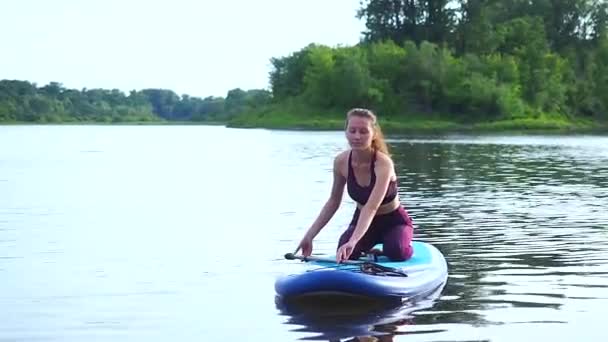 Жінка штовхає і тягне весло крізь сяючу поверхню води і провідну дошку в сонячний ранок — стокове відео