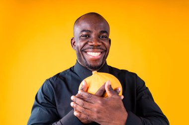 İnsanlar ve Cadılar Bayramı hazırlık konsepti, stüdyonun sarı arka planında küçük bir balkabağı tutan adam.